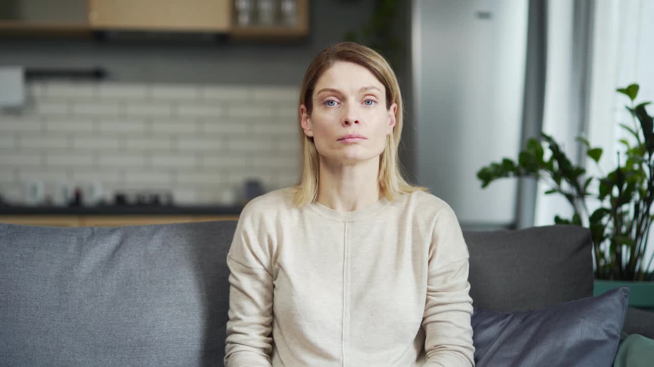 Сonfident woman looking at camera and having video chat conversation while sitting on sofa at home. Webcam view of middle-aged female talking to interlocutor during virtual meeting视频素材