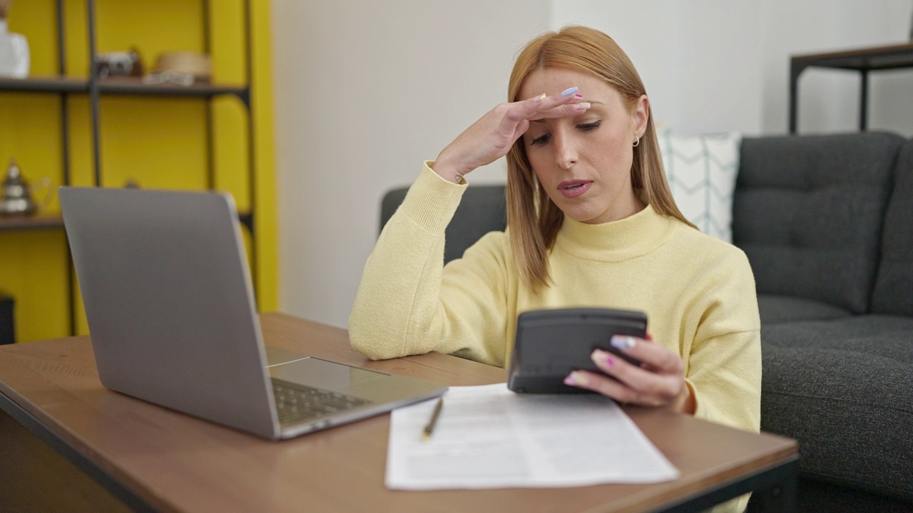 年轻的金发女人在家里用笔记本电脑记账视频素材