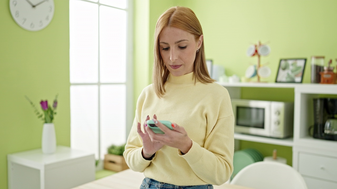 年轻的金发女子站在家里用智能手机视频素材