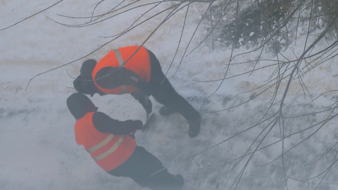 工人们在冬天清扫道路上的积雪。清理道路和街道上的冰雪。城市服务部门在暴风雪后用铲子清理积雪。视频素材