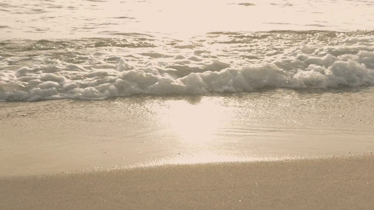 日出时海浪冲击着海滩上的沙子。视频素材