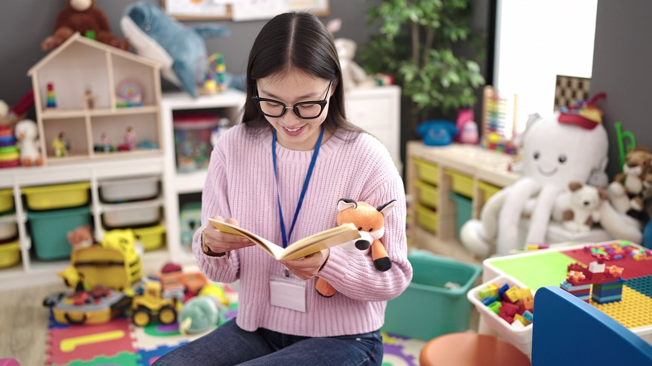 年轻的中国女幼儿教师坐在幼儿园的桌子上读故事书视频素材