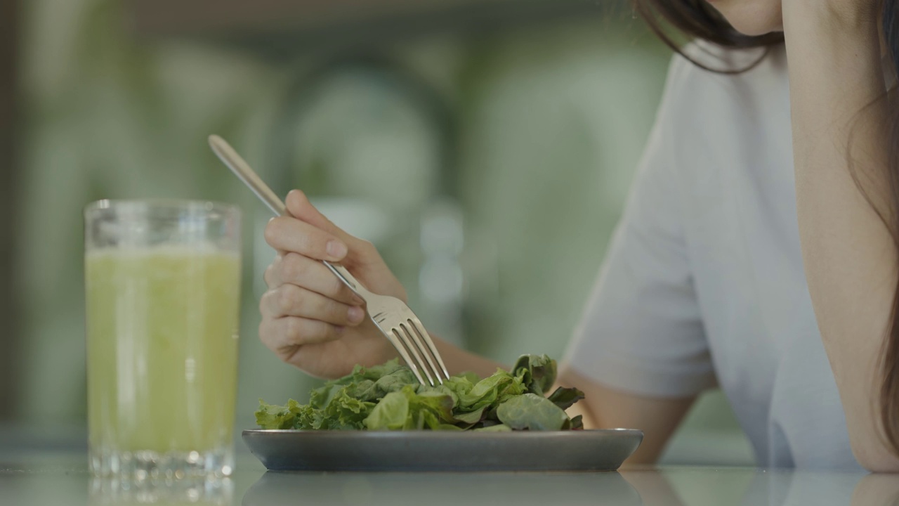 悲伤的女孩试图吃沙拉和健康的食物。女孩不喜欢吃生菜叶。慢动作视频素材