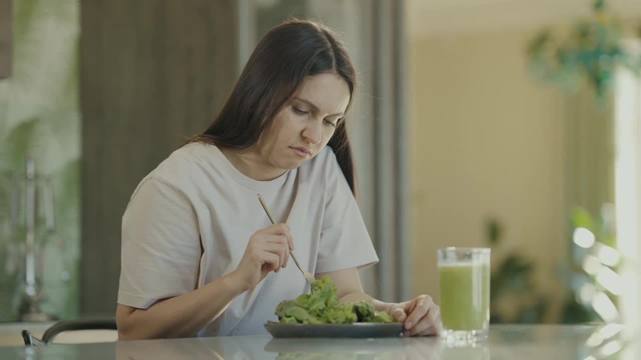 不开心的节食女孩看着盘子里的沙拉和蔬菜奶昔。健康饮食和饮食的概念。慢动作视频素材