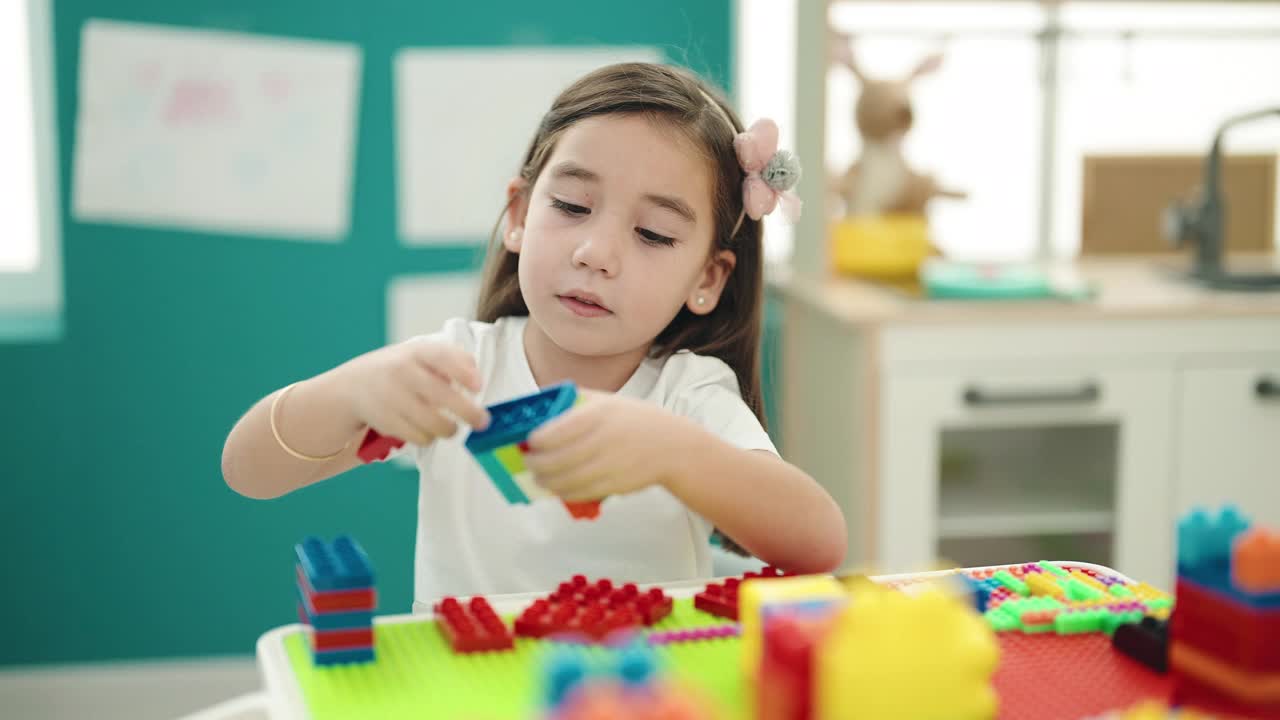 可爱的西班牙女孩坐在幼儿园的桌子上玩积木视频素材