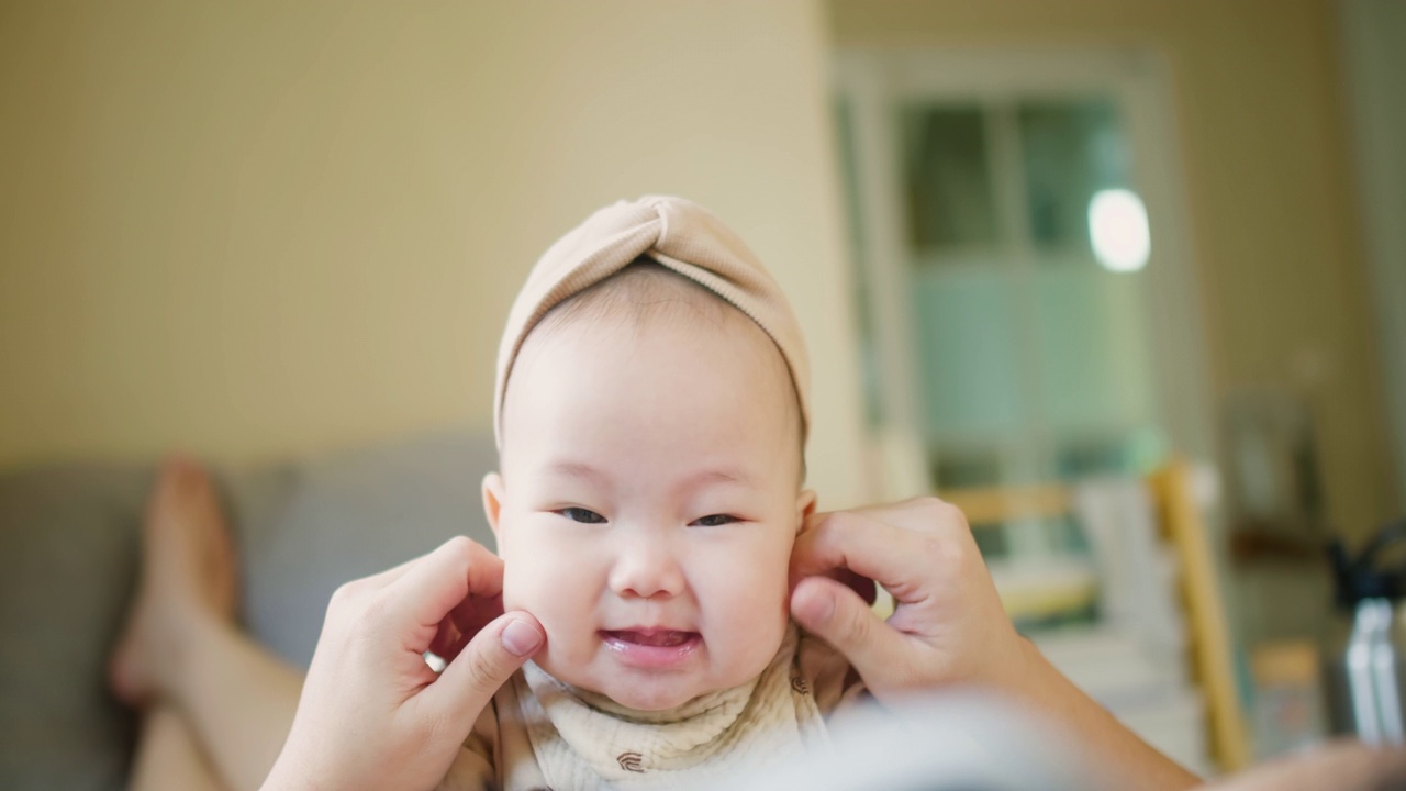 快乐的妈妈和宝宝一起在客厅玩亲密活动。小可爱的亚洲婴儿婴儿女孩兴奋的笑和有趣的花时间在沙发上的家庭在家里玩得很开心视频素材