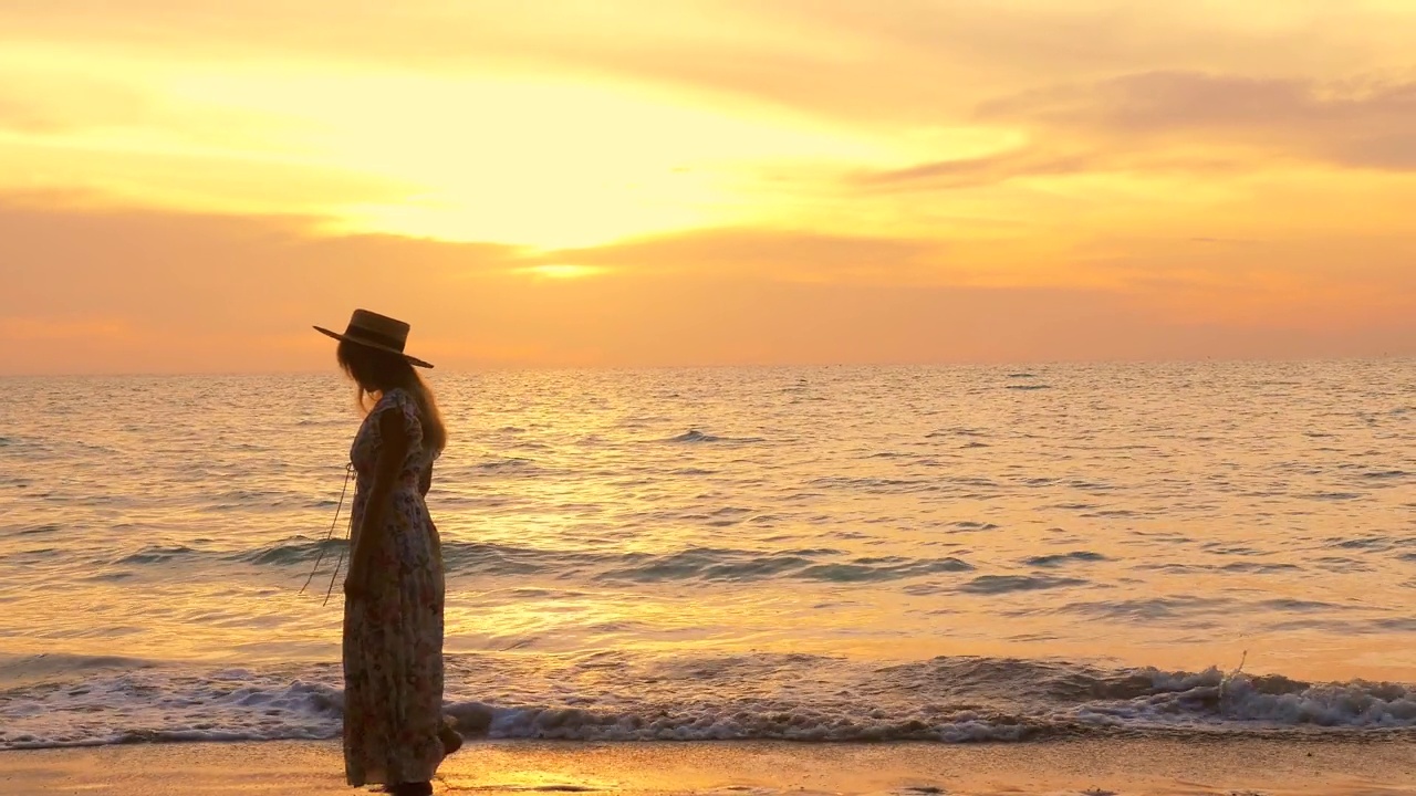 在金色的夕阳下，穿着漂亮裙子的女人沿着海滩散步视频素材