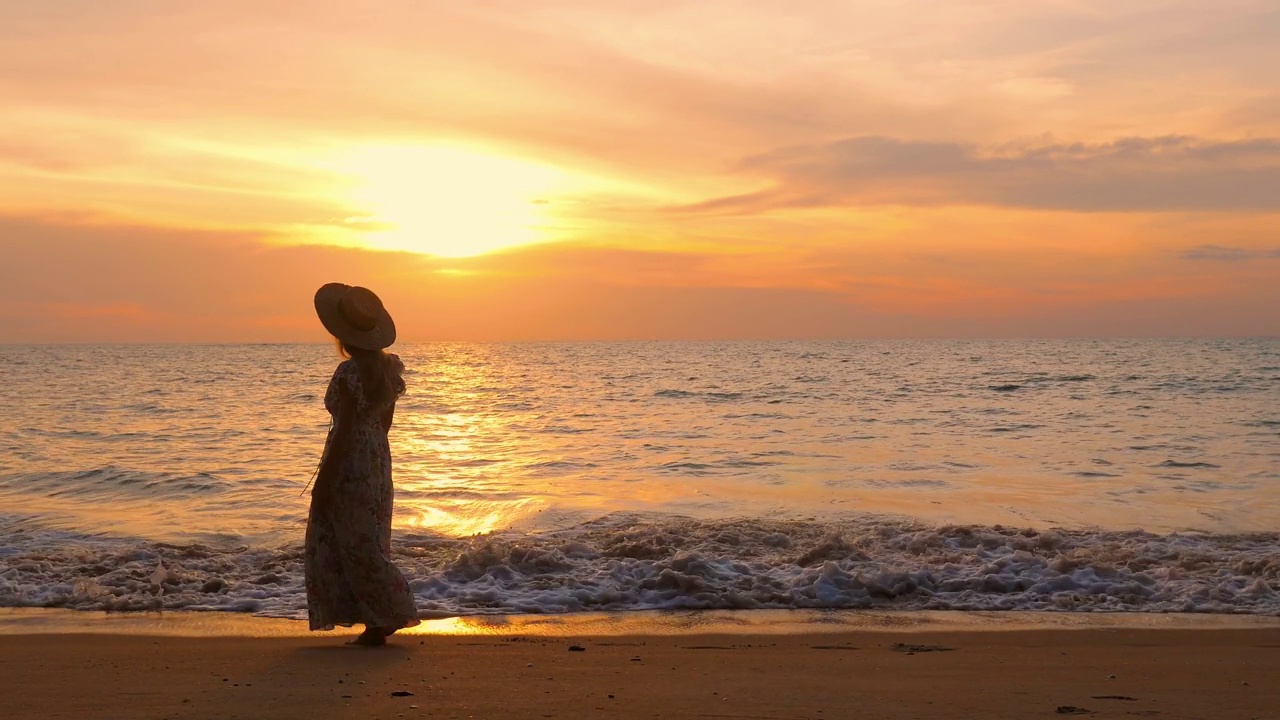 在金色的夕阳下，穿着裙子的女人走在海滩上视频素材