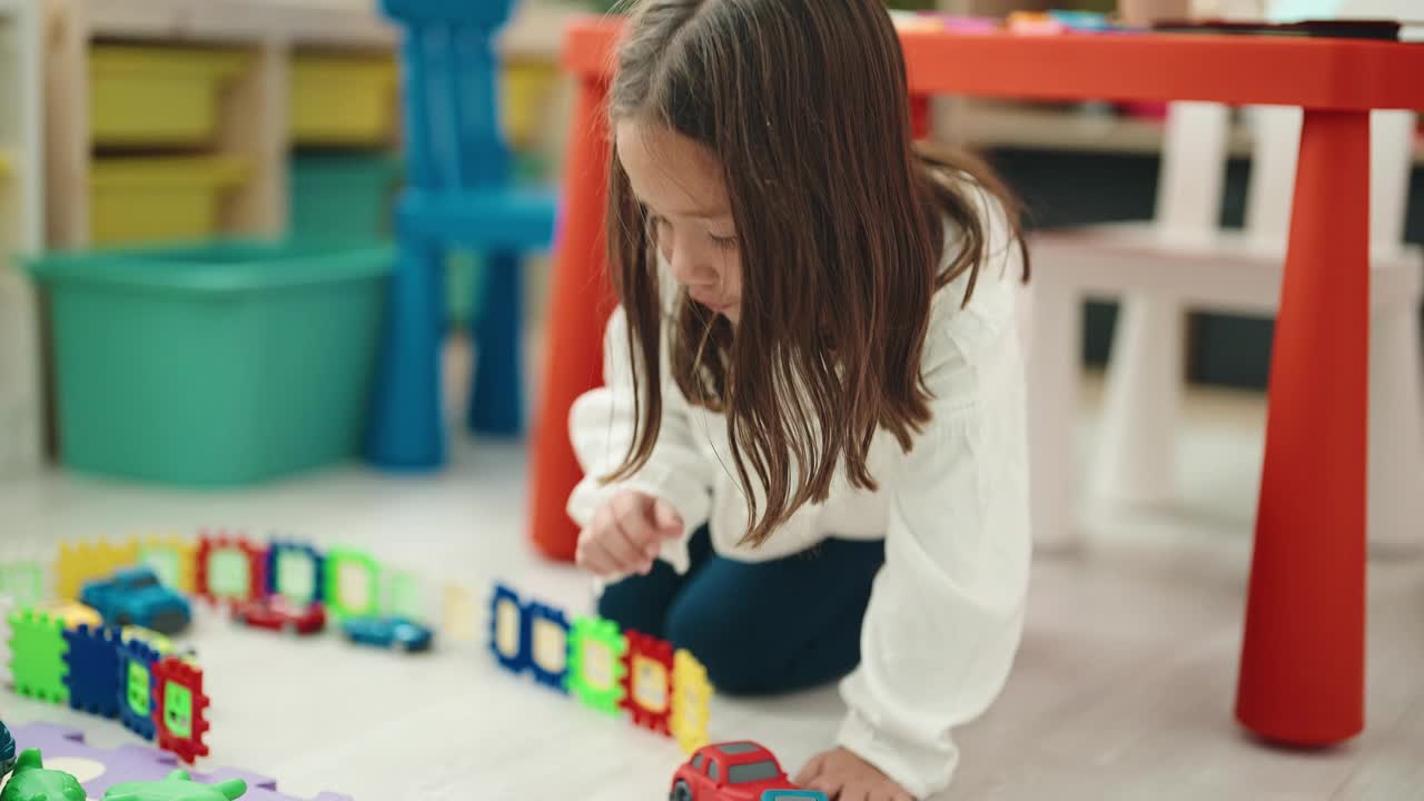 可爱的西班牙女孩坐在幼儿园的地板上玩汽车玩具视频素材