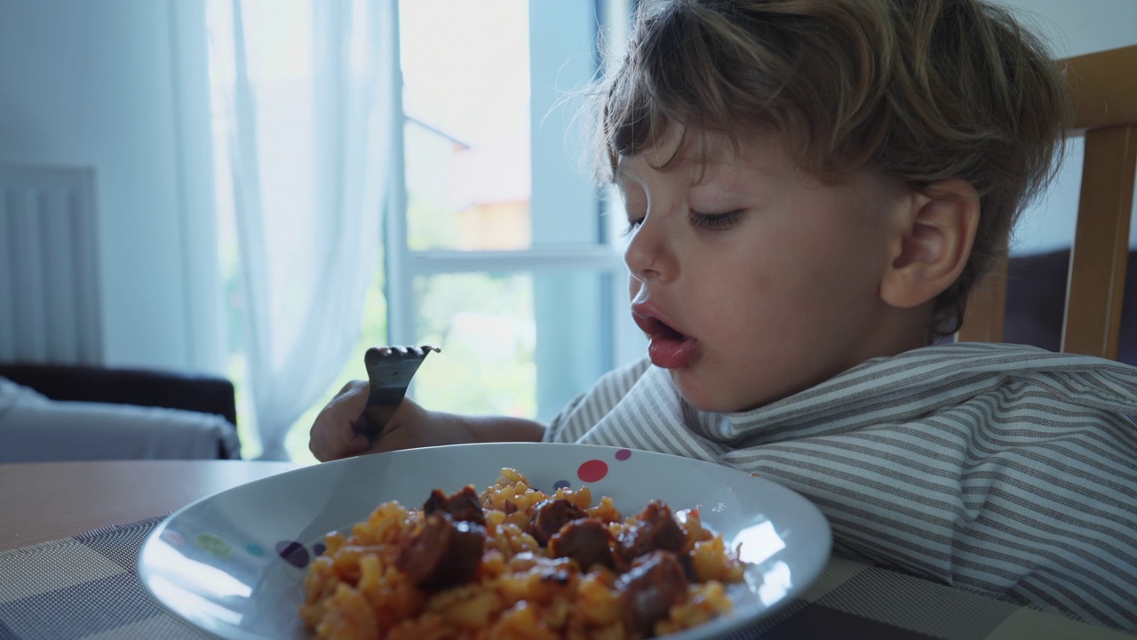 孩子吃热的食物烫伤嘴。一个小男孩把意大利面吐在盘子里。孩子吃午饭视频素材