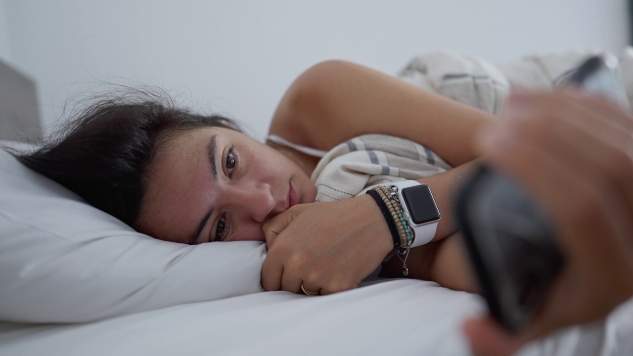 女子躺在床上看智能手机。沉迷于现代科技的女性。成年女孩早上第一件事就是盯着屏幕看短信视频素材