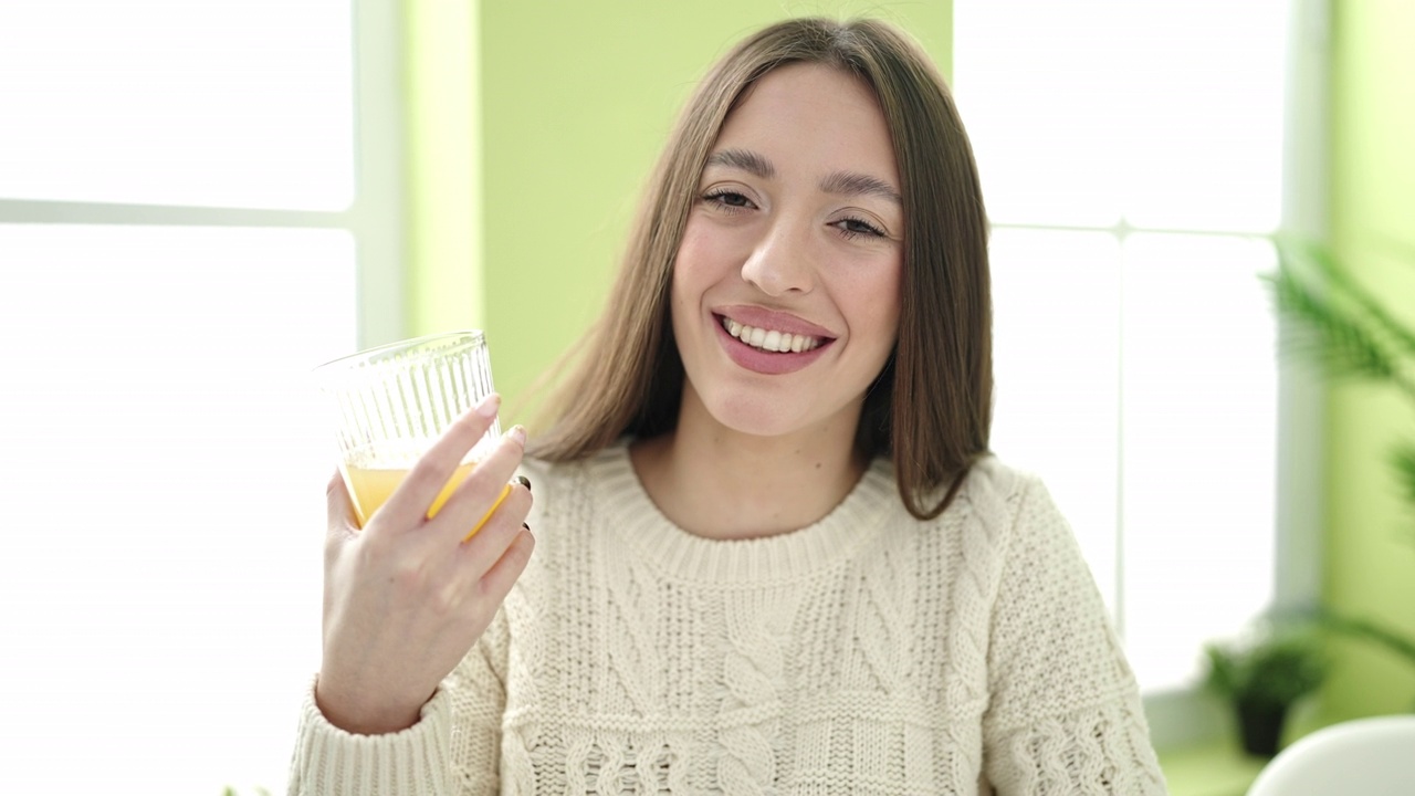 年轻美丽的西班牙女子拿着一杯橙汁坐在家里的桌子上视频素材