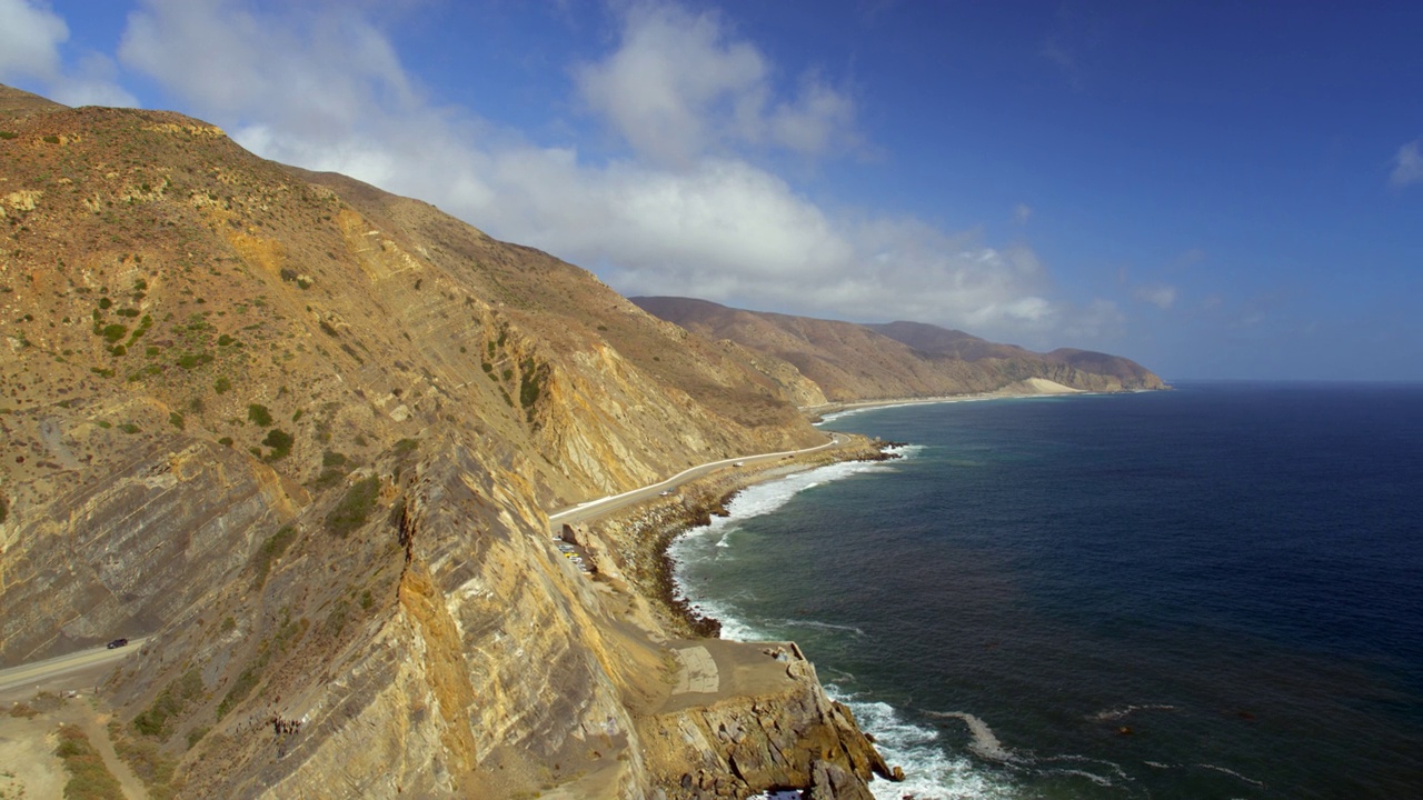 在阳光明媚的日子里，汽车在美丽的山和波浪般的海的道路上移动的空中向后拍摄-加利福尼亚州卡马里略视频素材