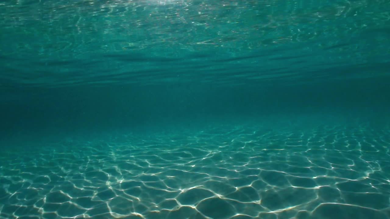 阳光穿透海水，带着柔和的波浪和运动，在沙滩上形成的水下光纹视频素材