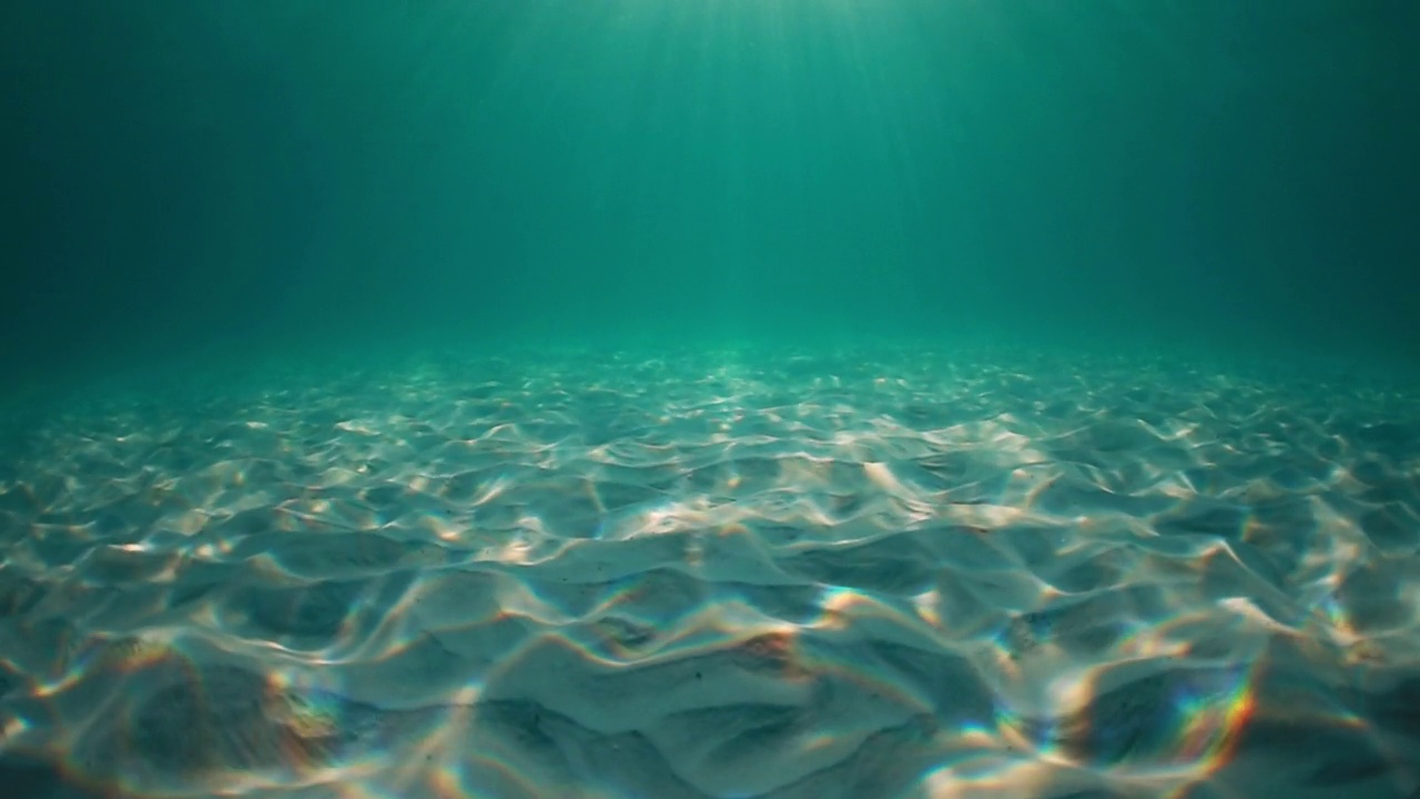 阳光穿透海水，带着柔和的波浪和运动，在沙滩上形成的水下光纹视频素材