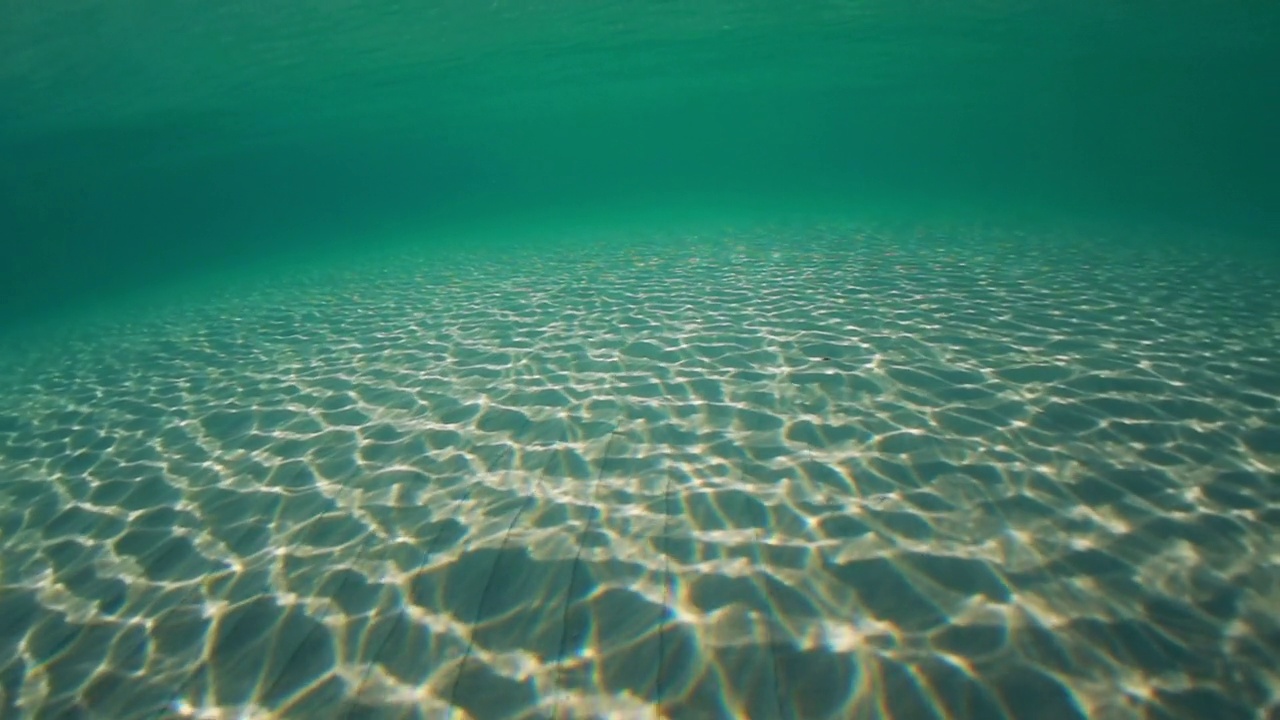 阳光穿透海水，带着柔和的波浪和运动，在沙滩上形成的水下光纹视频素材