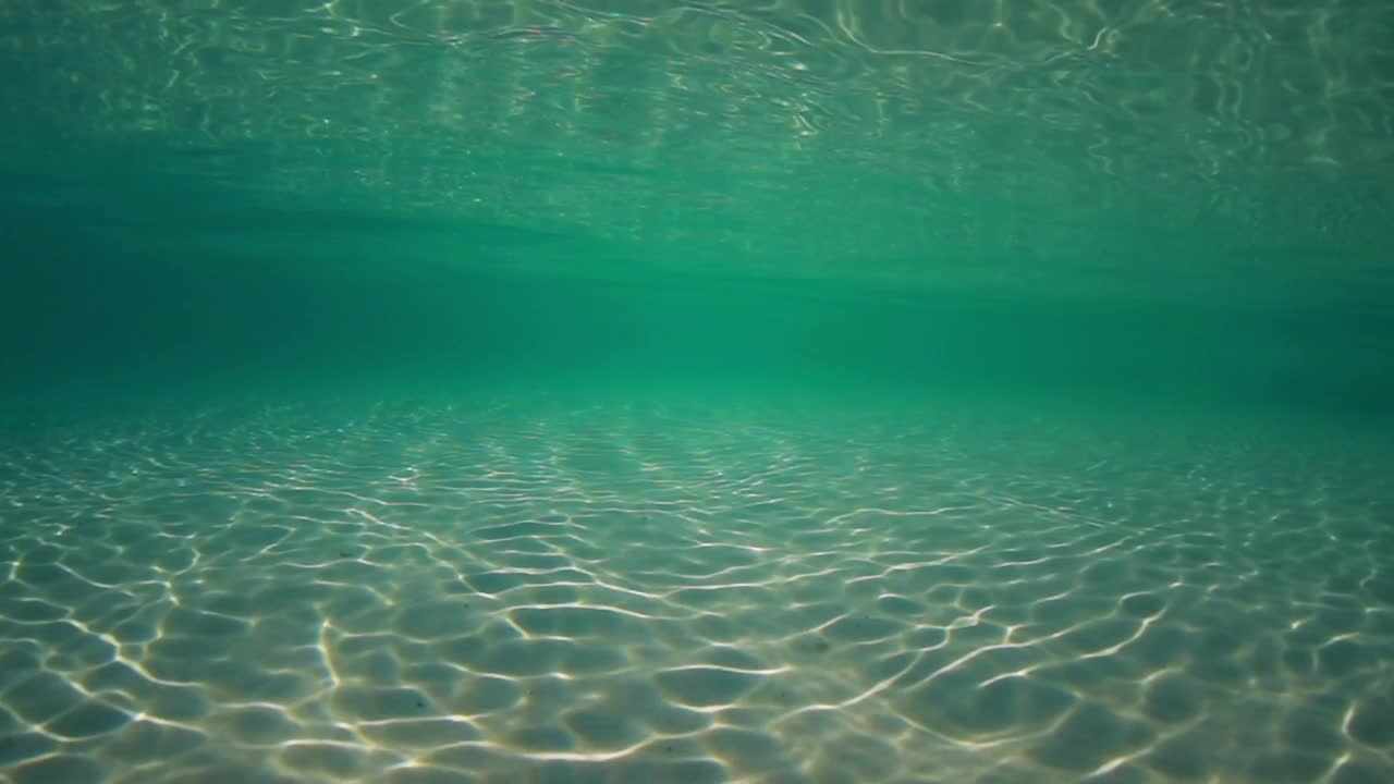 阳光穿透海水，带着柔和的波浪和运动，在沙滩上形成的水下光纹视频素材