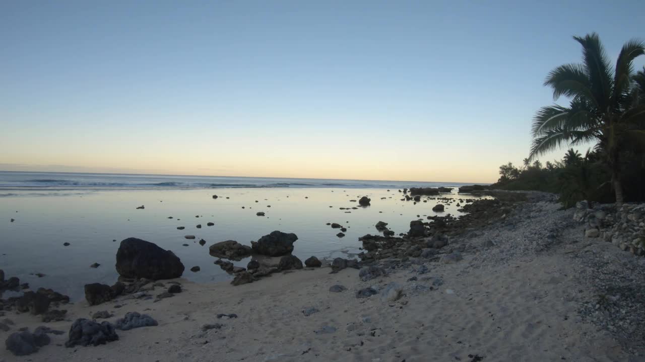 手持静止的海洋海岸线海湾沙质岩石海滩和椰子树，在日落黎明时分，在泻湖和平蛤水波内，眺望东太平洋的地平线视频素材