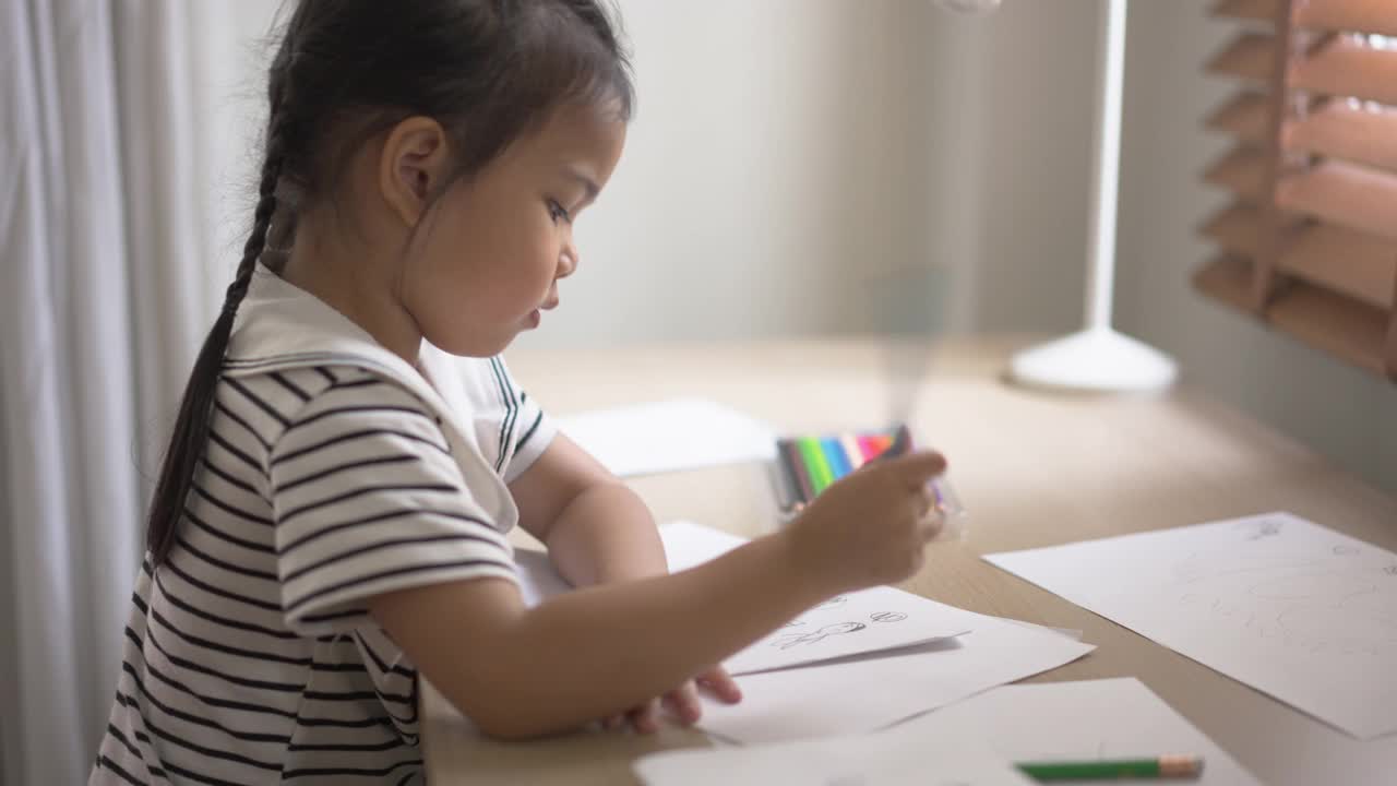 小女孩在书桌前的纸上画画。孩子在家里接受艺术教育视频素材