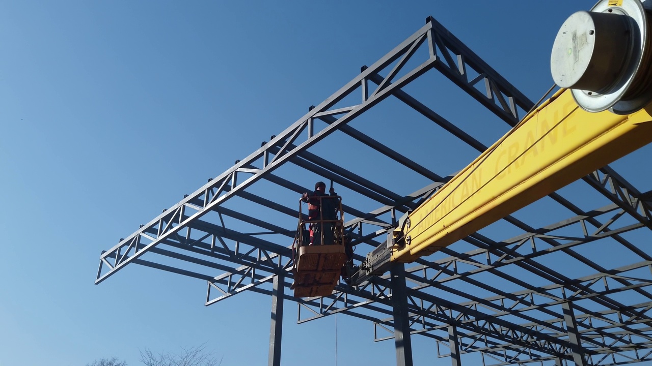 高空作业平台上的工人正在建造一座大型建筑物屋顶的金属结构视频素材