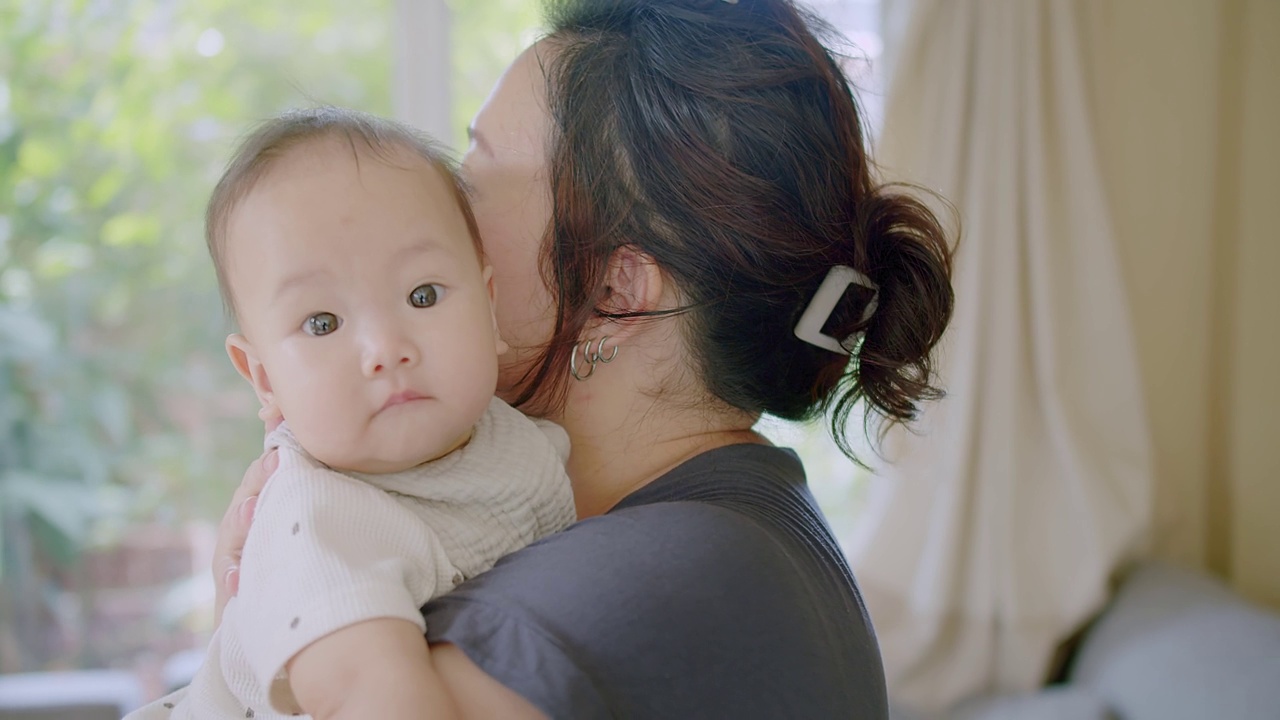 近距离肖像年轻妈妈抱抱抱抱小女婴可爱的小婴儿学步，可爱的亚洲妈妈抱抱小婴儿孩子，放松享受温柔的家庭时刻母性概念视频素材