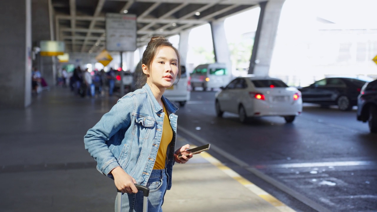 亚洲年轻女性乘客在机场前等待出租车。有吸引力的漂亮女人，游客，感觉快乐和兴奋去国外旅行从飞机假期旅行。视频素材