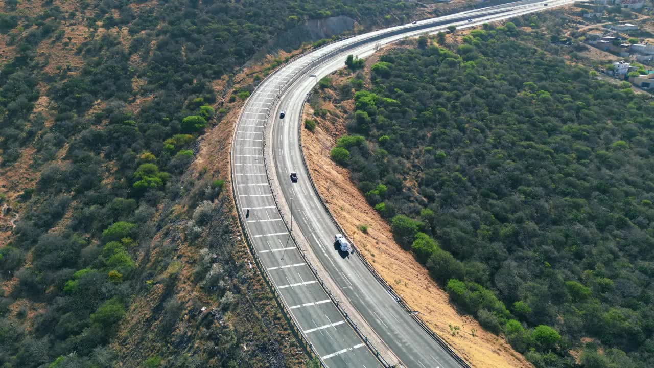 无人机拍摄的车辆行驶在公路上，沿着绿色的树木和清晨的阳光向上行驶视频素材