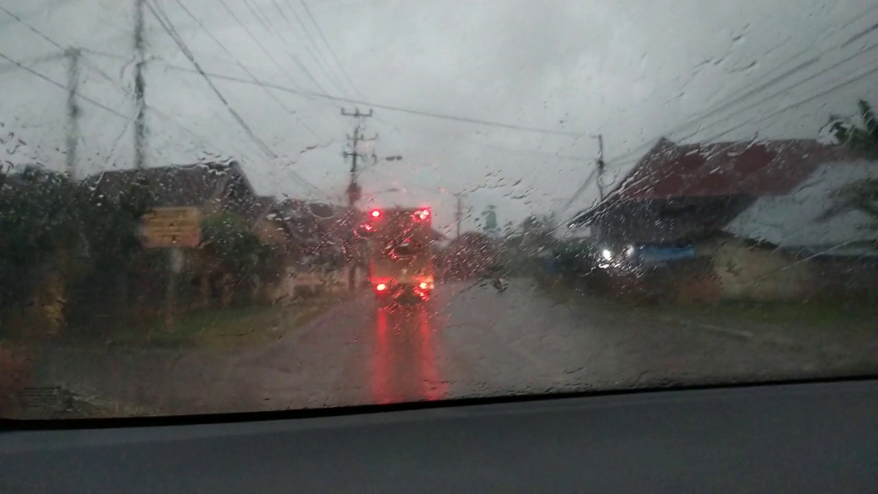 印尼村庄的道路交通，透过车窗，大雨滴在雨中行驶。雨中从汽车挡风玻璃看窗外视频素材