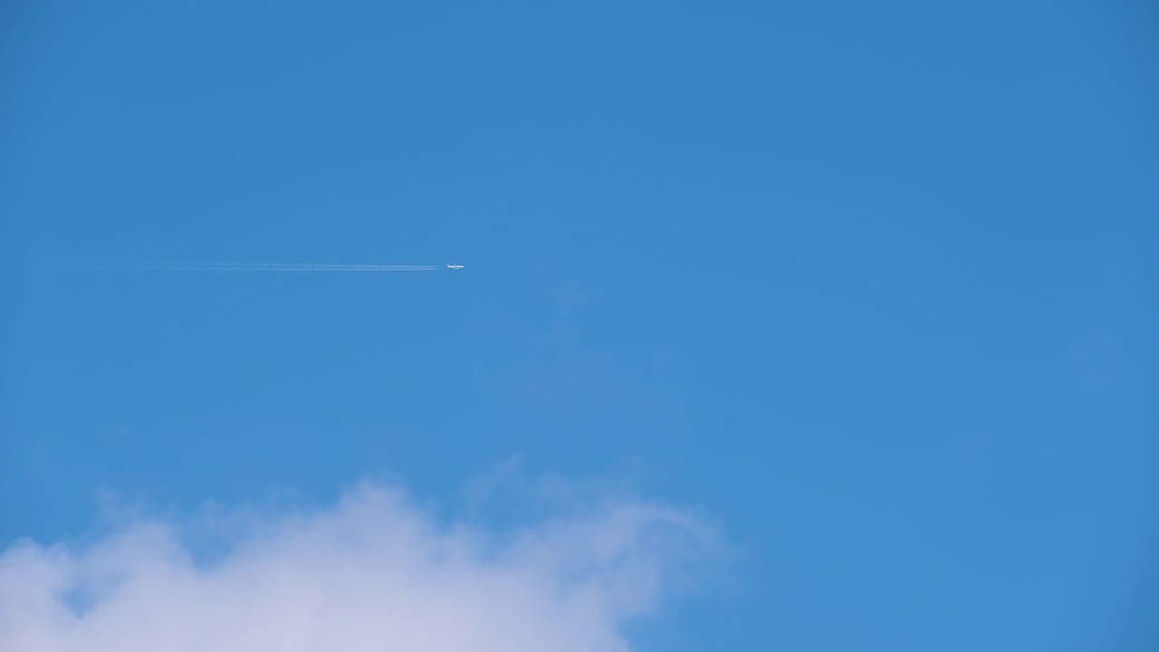 远处的客机在蓝天白云的高空飞行，留下了烟雾的痕迹。空中旅行概念视频素材