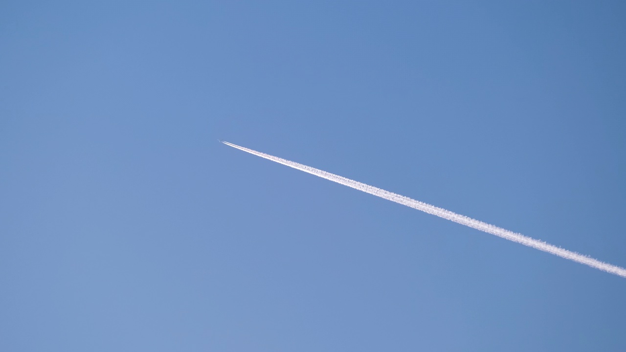 远处的客机在晴朗的蓝天上高空飞行，留下了白色的烟雾痕迹。航空运输概念视频素材