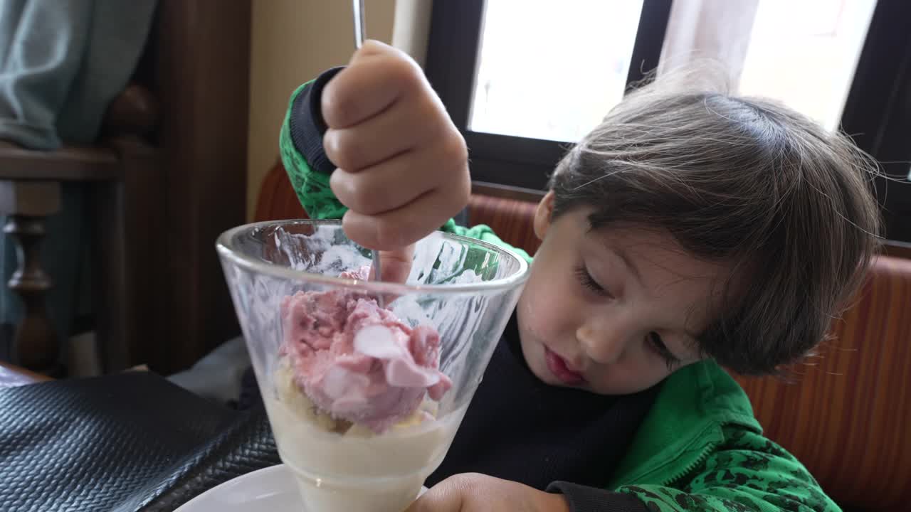 小孩用勺子在碗里吃冰淇淋。孩子午餐后坐在餐厅吃甜点视频素材