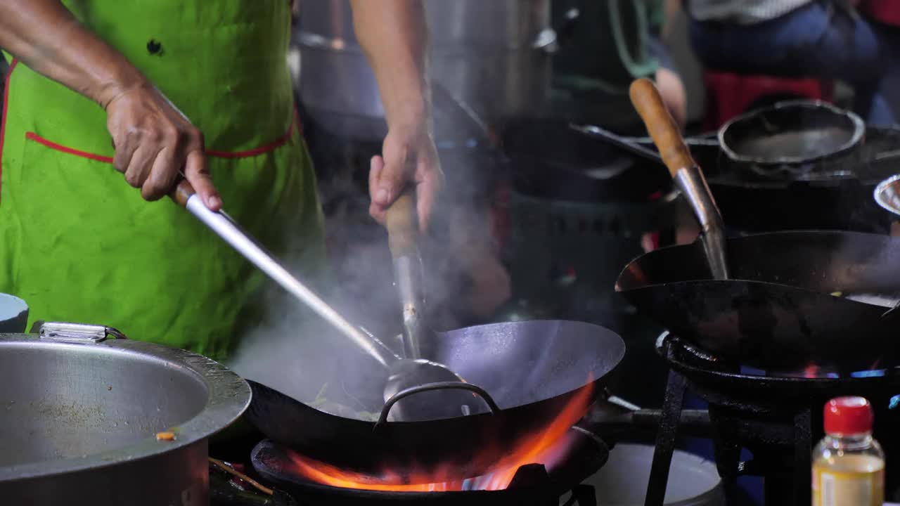 曼谷唐人街路边的炒锅起火。在泰国市中心的Yaowarat路美食街，厨师晚上在外面的路上烧热油和蔬菜。视频素材