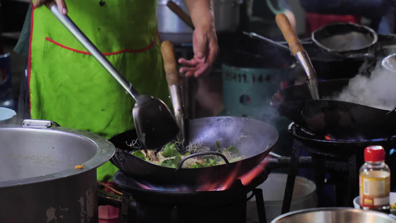 曼谷唐人街路边的炒锅起火。在泰国市中心的Yaowarat路美食街，厨师晚上在外面的路上烧热油和蔬菜。视频素材