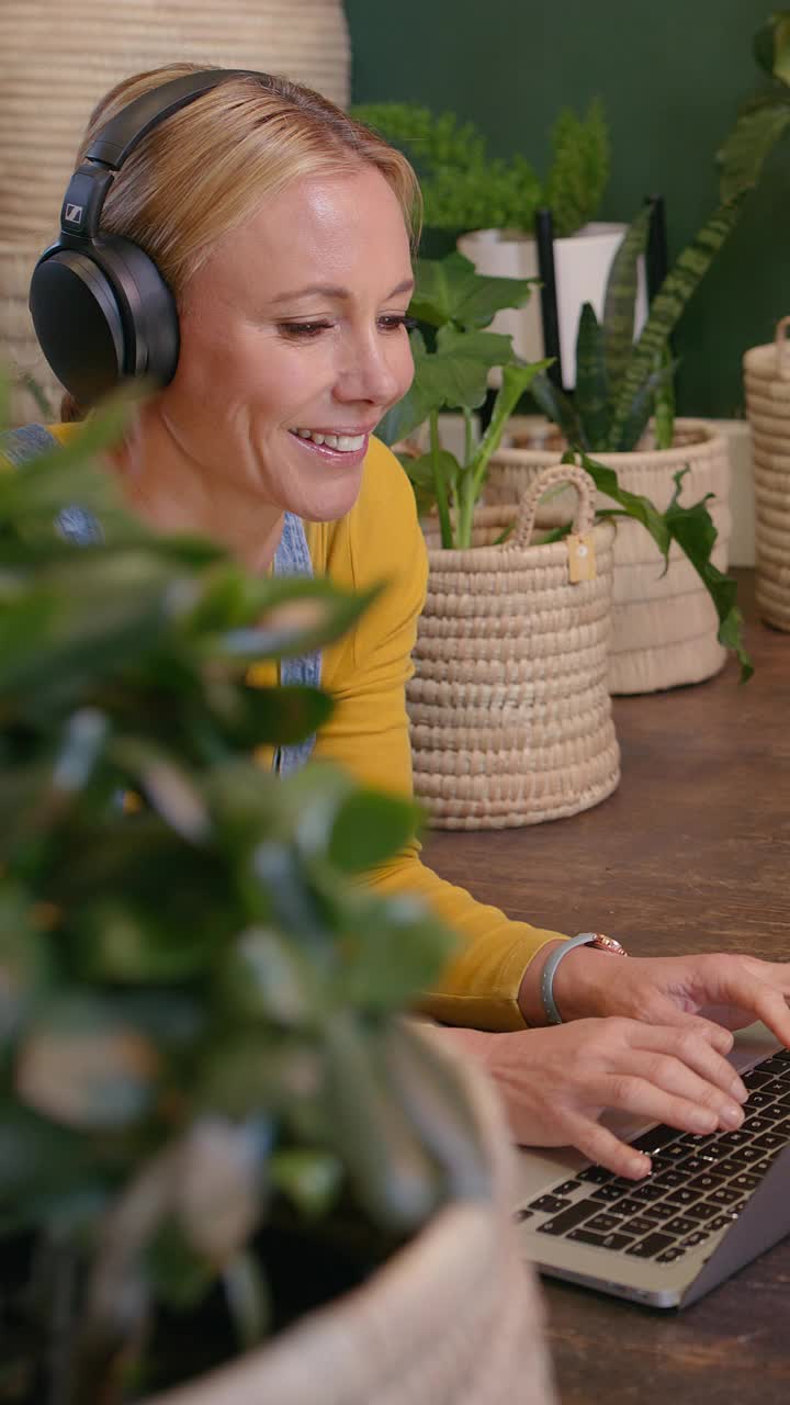 植物，耳机和笔记本电脑上的快乐女人，放松在地板上与健康播客，音频流媒体和打字。禅宗，和平和创意，成熟的人与音乐技术在波西米亚或生态房间视频素材