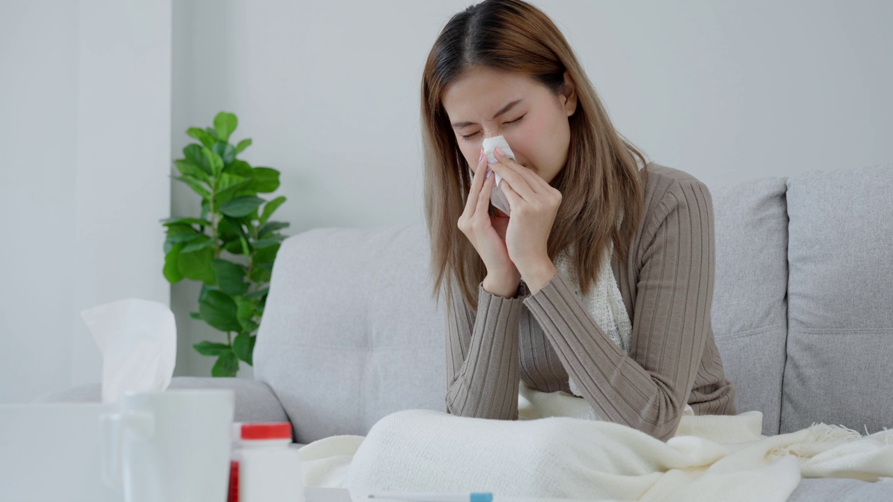 年轻的亚洲女性高烧，同时检查体温，女性打喷嚏和流鼻涕与季节性流感，过敏，数字体温计，病毒，冠状病毒，疾病，呼吸道视频素材