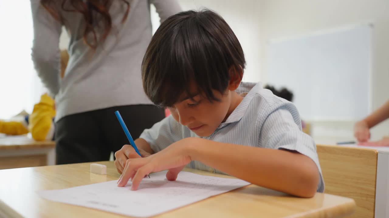 可爱的学生在小学教室里跟着老师学习。在幼儿园，聪明聪明的孩子们坐在桌子上，在纸上画画，在快乐和有趣的活动中学习艺术。视频素材