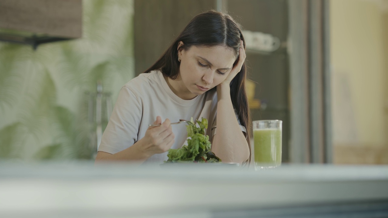 节食的悲伤女孩看着盘子里的生菜叶子，把它们钉在叉子上。特写镜头。慢动作视频素材