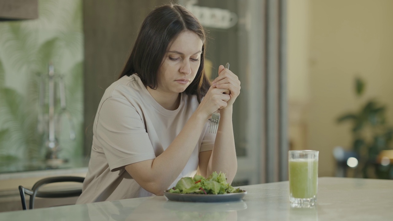 沮丧的女孩坐在桌旁，看着盘子里的生菜叶子。女孩不想节食。慢动作视频素材