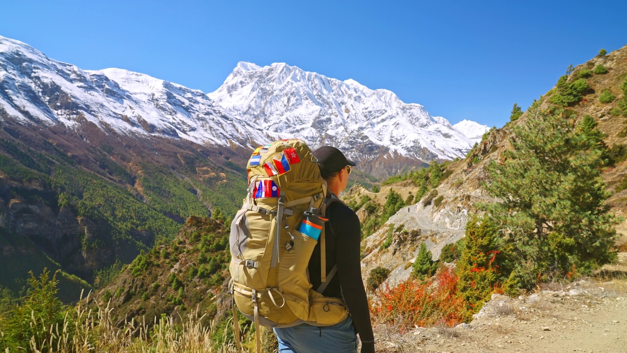 背包女旅行者在步道上徒步旅行，同时欣赏远处美丽的山景，尼泊尔安纳普尔纳环行视频素材