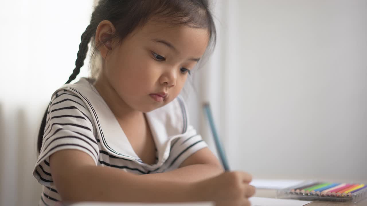 小女孩在书桌前的纸上画画。孩子在家里接受艺术教育视频素材