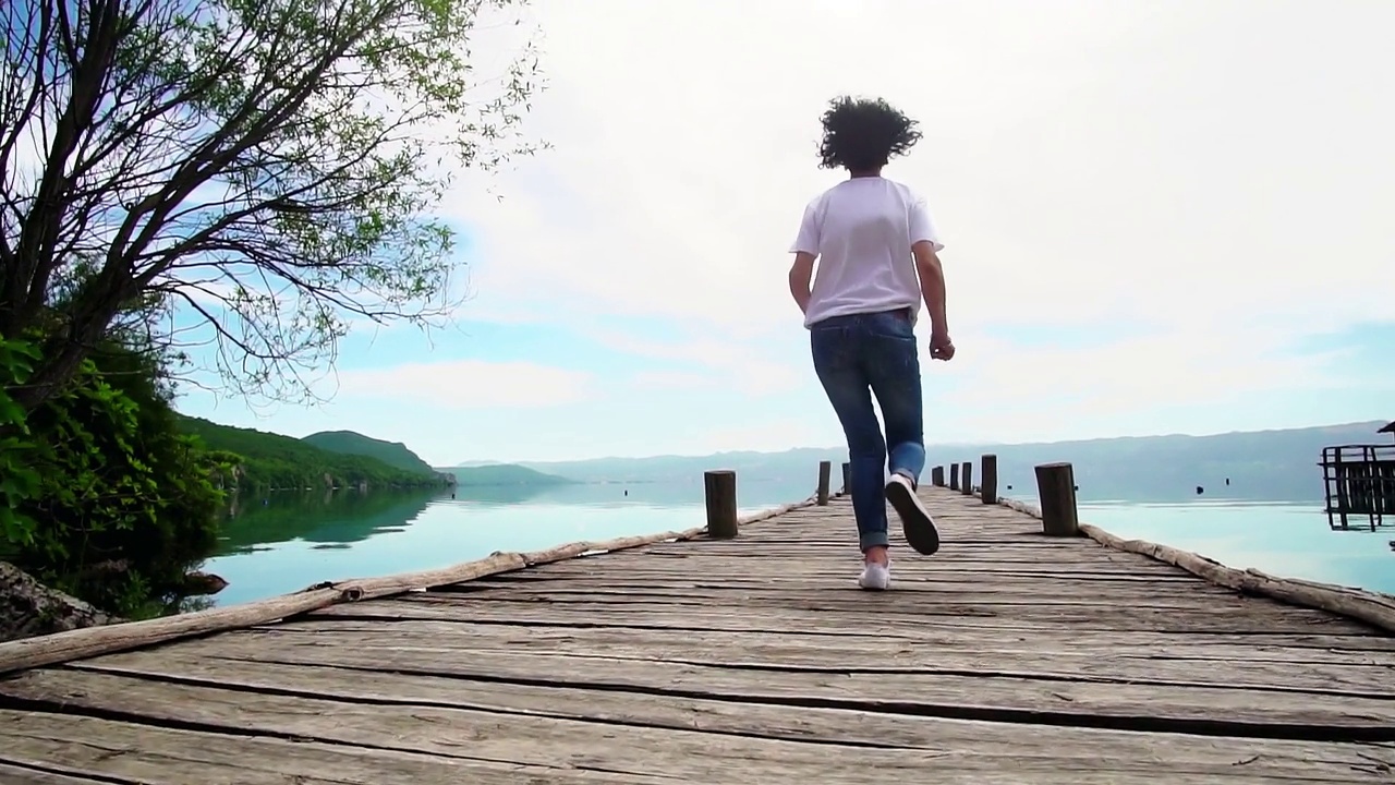 积极的女旅行者表现出胜利、成功的情绪，在木制码头上奔跑和跳跃，双手张开，慢动作视频素材