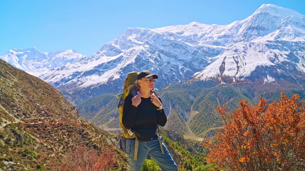 在一个阳光明媚的日子里，一名成年女性徒步旅行者在徒步途中休息，呼吸新鲜空气，背景是喜马拉雅山脉视频素材