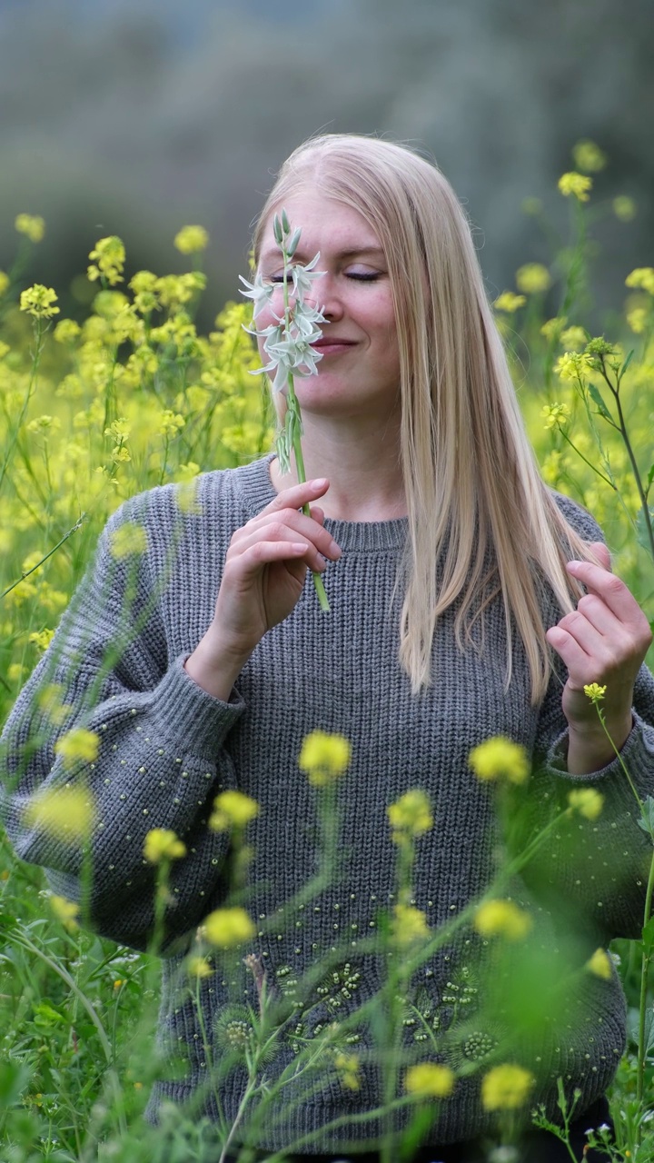 美丽的金发女人闻到春天的花朵视频素材