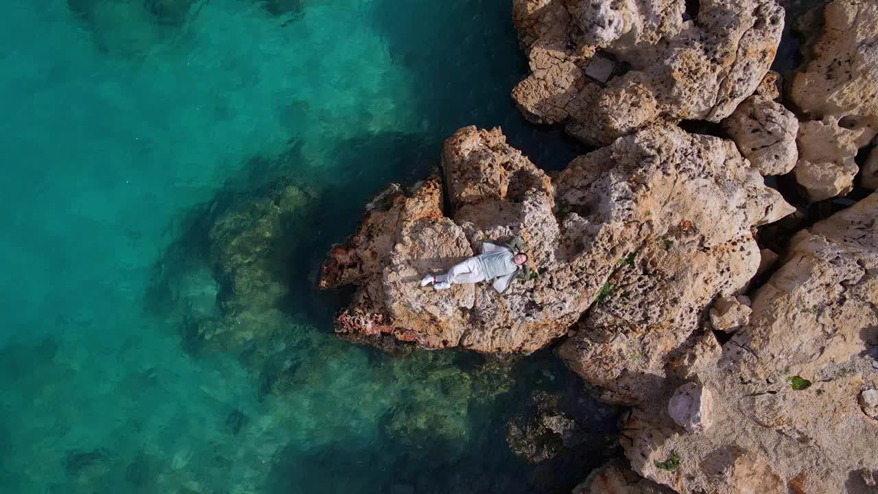 鸟瞰图的女人放松地躺在温暖的石头在岩石海岸视频素材