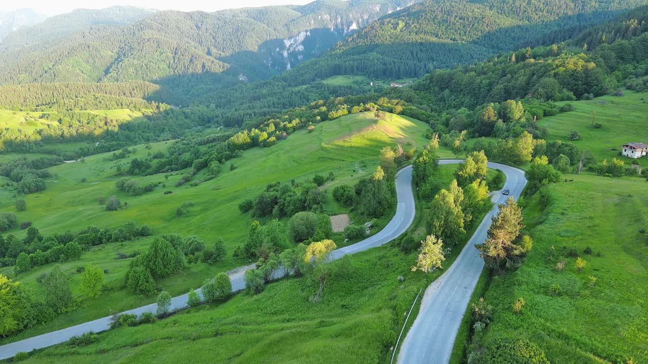 一条路经过布满云杉森林和草地的山丘，映衬着多云的天空视频素材