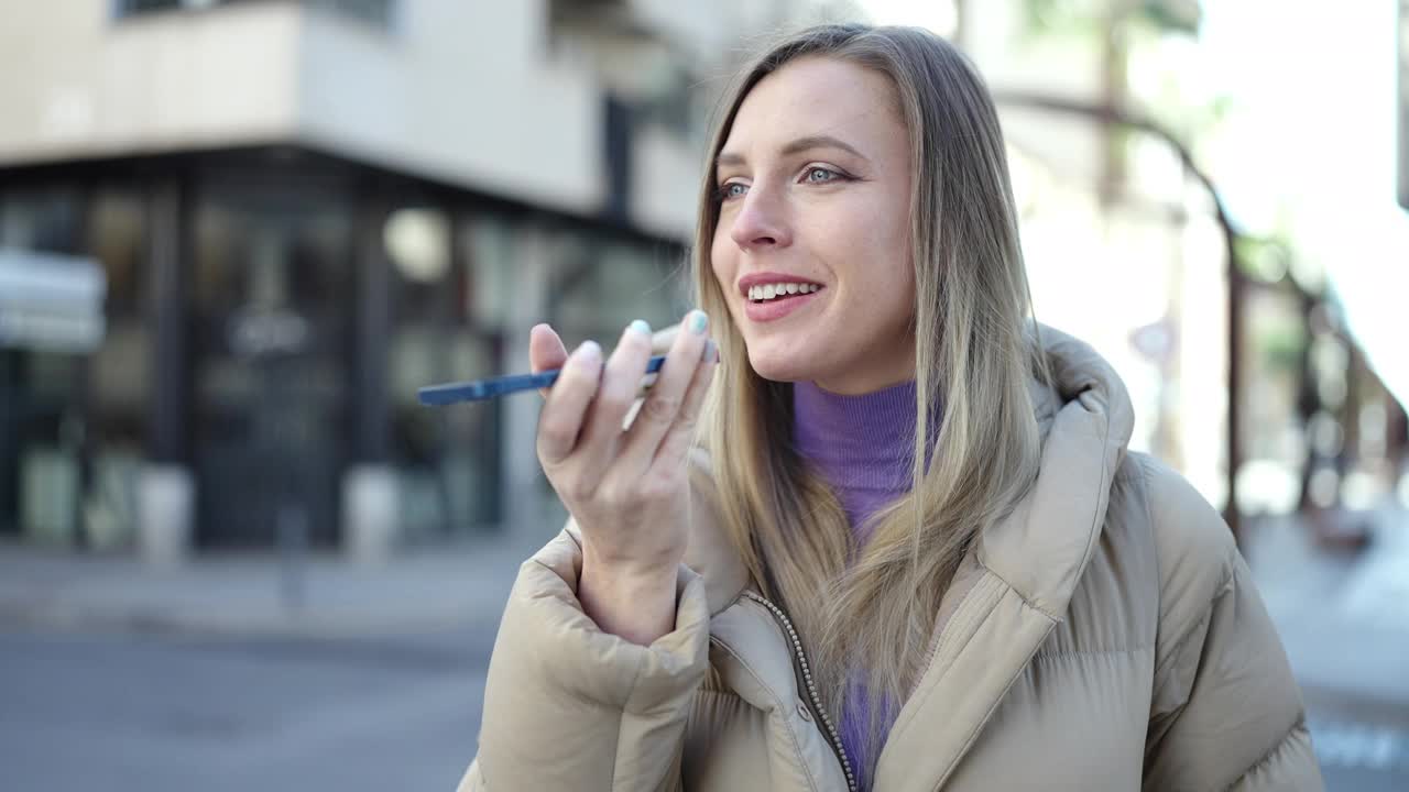 年轻的金发女子微笑自信地在街上通过智能手机发送语音信息视频素材