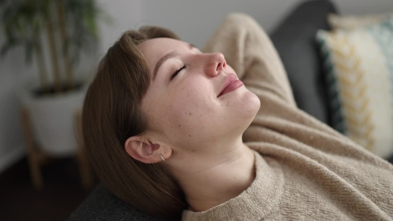 年轻的金发女人放松的手在头上坐在家里的沙发上视频素材