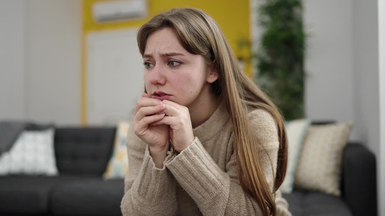 年轻的金发女子紧张地坐在家里的沙发上视频素材