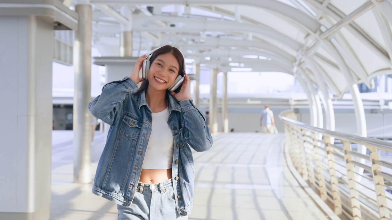 年轻的亚洲女子用耳机听好听的音乐，在城市里散步。女孩幸福，微笑面对。女人喜欢听能让她放松和享受生活的音乐视频素材