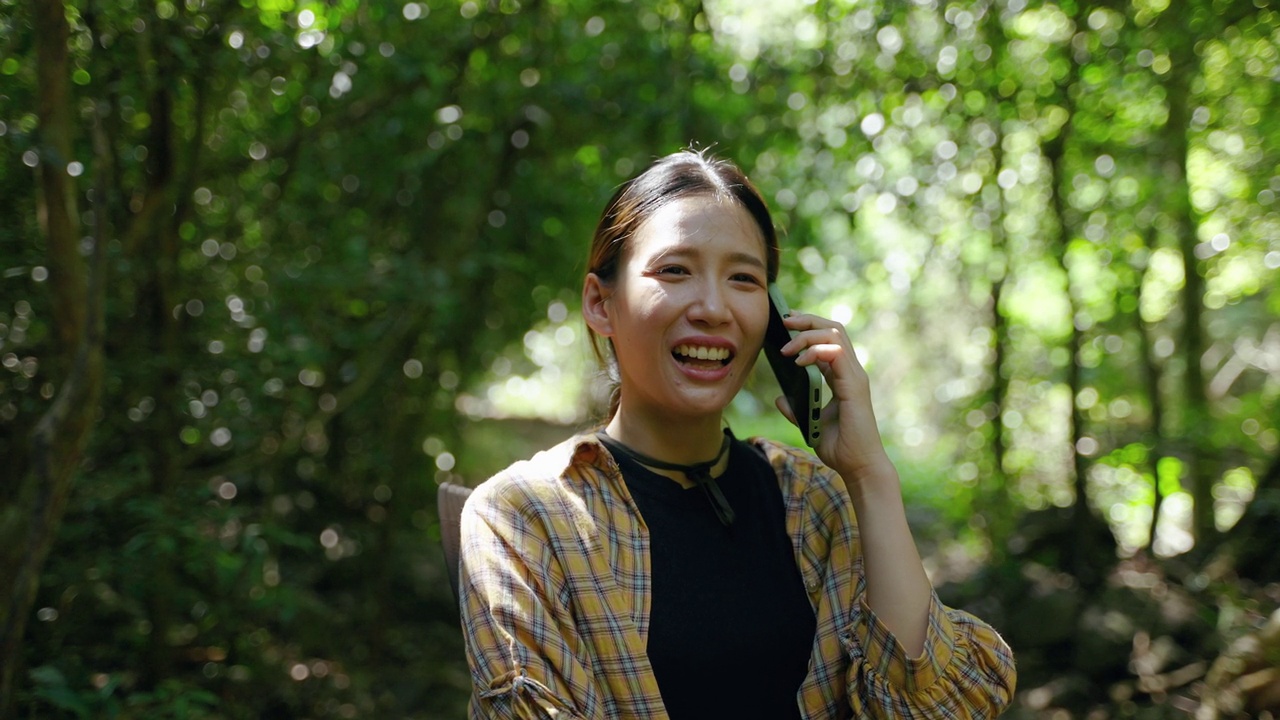 年轻的亚洲女性在热带雨林中使用手机与朋友交谈，无界的通信概念，技术和通信视频素材